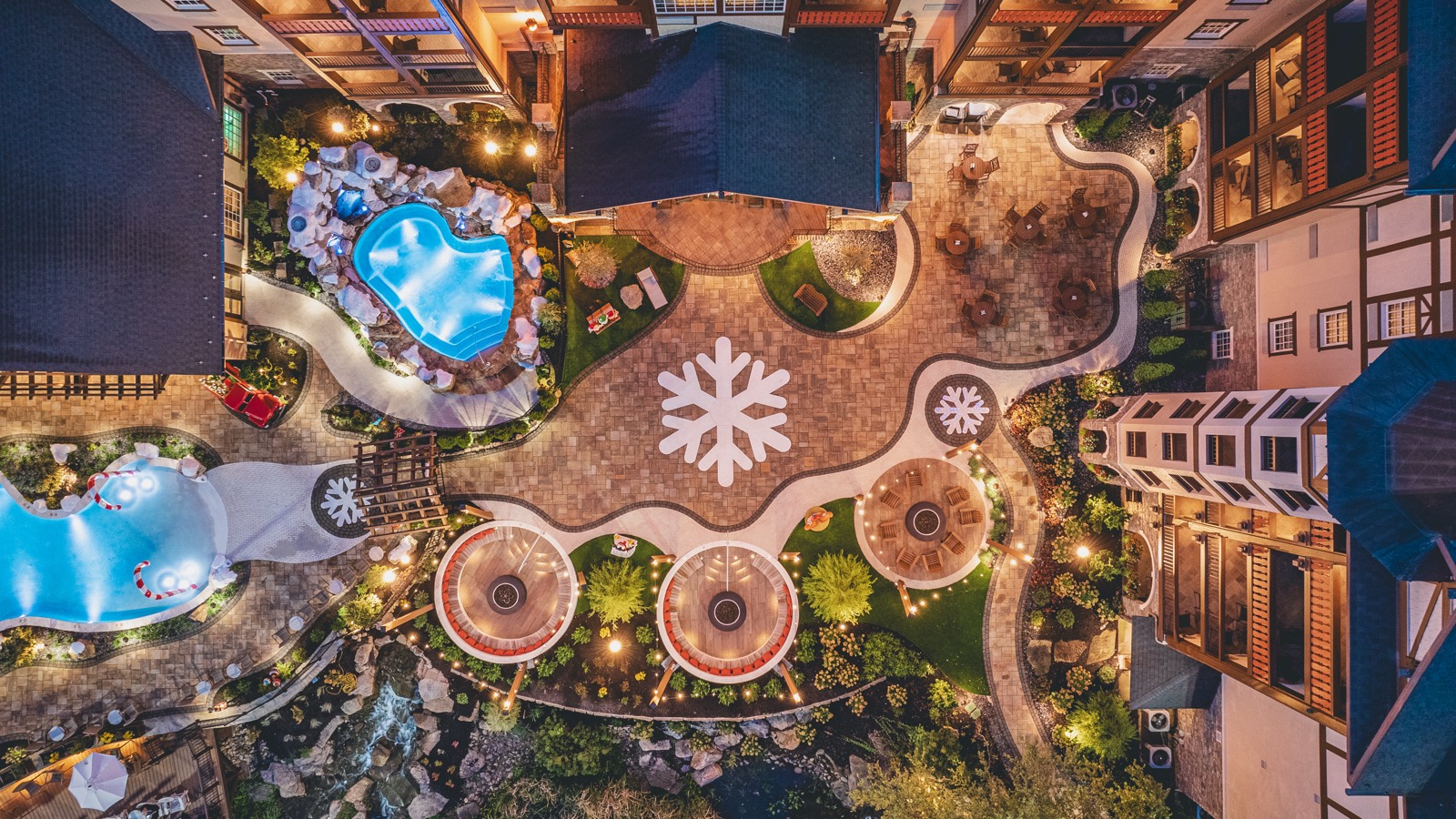 The finished Snowflakes in the Smokies plaza at dusk in Pigeon Forge: a custom paver snowflake mosaic, lit fire-pit circles and resort pools, built by Morales Outdoor Living