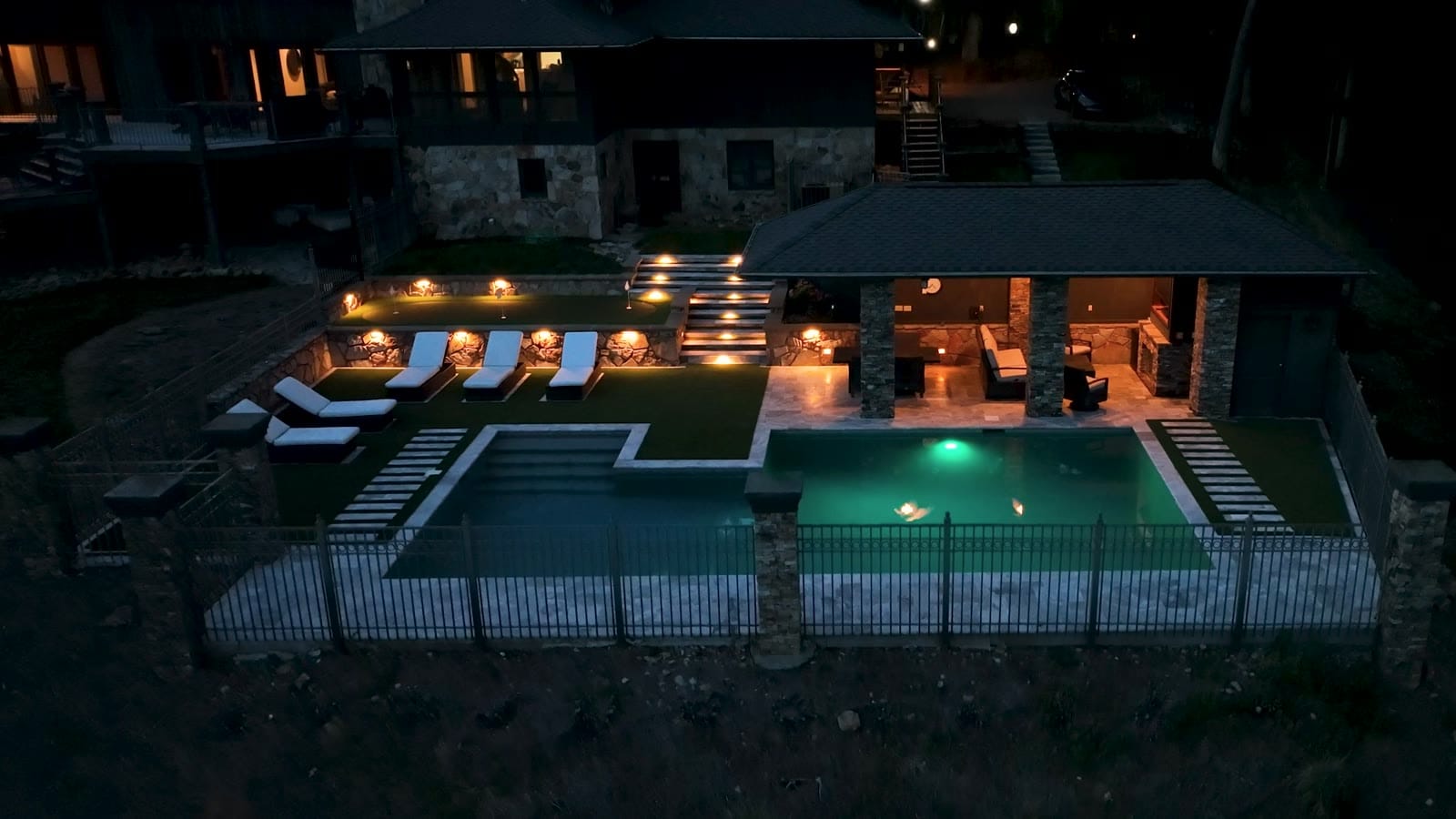 A finished Morales Outdoor Living backyard at night: lit steps, pavilion, and pool